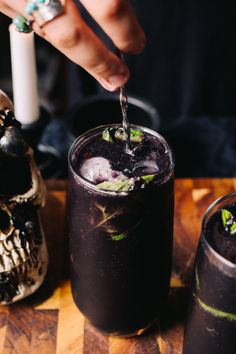 someone is pouring something into a glass with ice and mint on the table next to two skulls