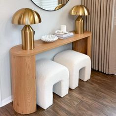 a wooden table topped with two white stools next to a round mirror and lamp