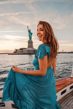 a woman in a blue dress is standing on a boat near the statue of liberty