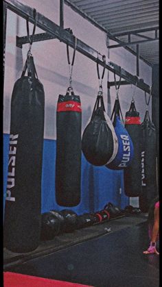 boxing bags hanging from the ceiling in a gym with other punching gloves on display behind them