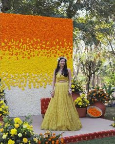 a woman wearing a yellow dress standing in front of an orange and yellow flower display