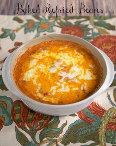 baked refried beans in a white bowl on a floral tablecloth with the words baked refried beans above it