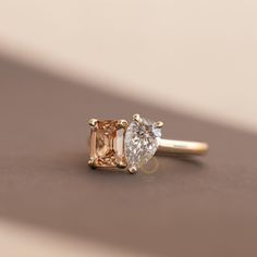 an engagement ring with two different colored stones on it's side, sitting on top of a table