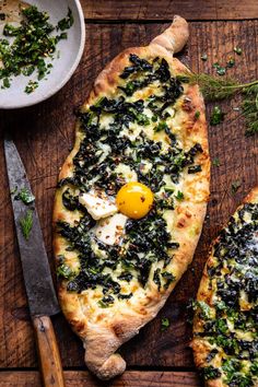 two pizzas with spinach and an egg on them sitting on a wooden table