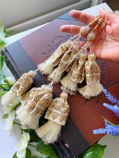 a hand is holding some tassels on top of a book with flowers in the background