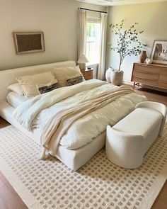 a large white bed sitting on top of a wooden floor next to a tall window