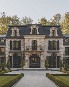 a large stone house with black shutters on the front and side windows, surrounded by hedges