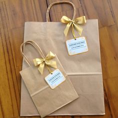 two brown paper bags with gold bows on them sitting on a wooden floor next to each other