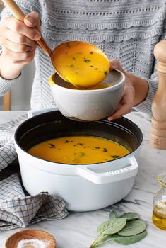 a woman is holding a spoon over a bowl of soup on a table with other ingredients