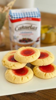 some cookies are on a white plate with strawberry jam in the middle and a carton of butter behind them