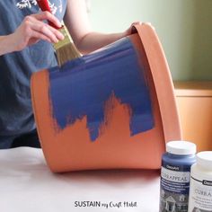 a person painting an orange bucket with blue paint