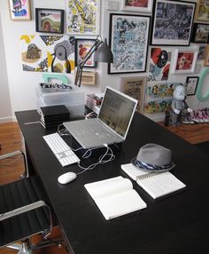 a desk with a laptop, mouse and other office supplies on it in front of a wall full of pictures