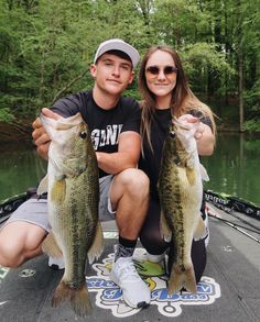 a man and woman holding two small fish on a boat in the water with trees in the background