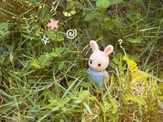 a small toy rabbit sitting in the middle of some tall green grass and plants,