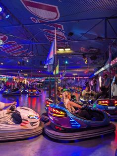 people ride bumper cars at an indoor amusement park with lights on the ceiling and blue lighting