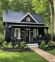 a small black house in the middle of some trees and grass with bushes around it