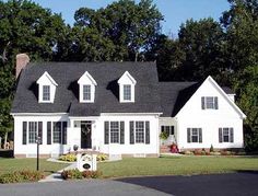 a white house with black shingles and two large windows on the front of it