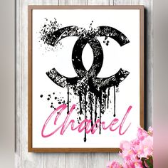 a pink and black chanel poster hanging on a wooden wall next to some flowers