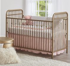 a baby crib with pink and white bedding next to a window