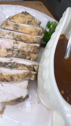 a white plate topped with meat next to a bowl of soup