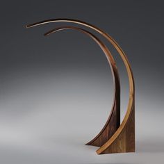 a wooden sculpture with curved sides on a grey background, it looks like an arc