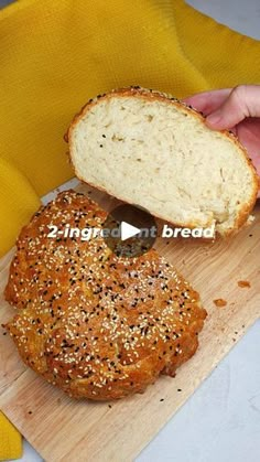 a person holding a piece of bread on top of a cutting board next to a loaf of bread