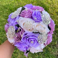 a bridal bouquet with purple roses and diable brooches is held in someone's hand