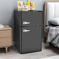 a black refrigerator freezer sitting in a bedroom next to a night stand and nightstand