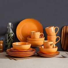 an assortment of orange dinnerware and utensils on a gray surface with grey walls in the background