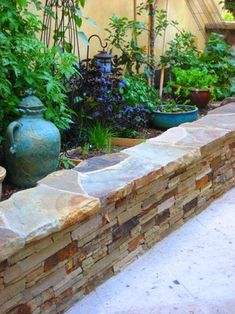 a stone wall in the middle of a garden with potted plants and other greenery