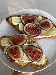 two pieces of bread with cheese and figs on them sitting on a white plate