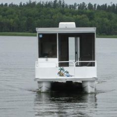 a small houseboat floating on top of a lake with trees in the back ground