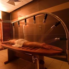 a woman laying on top of a wooden bench in a bathroom next to a shower