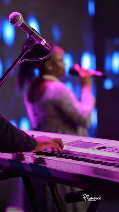 a woman sitting at a keyboard with a microphone in front of her and another person on the stage behind her