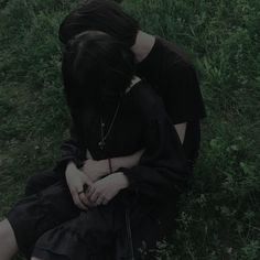 two people sitting in the grass with their heads on each other's shoulders,