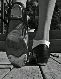 black and white photograph of person's feet with shoe on wooden decking area