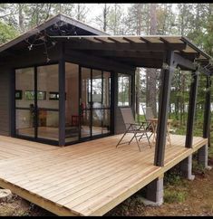 a wooden deck with chairs on it next to a small house in the woods and trees