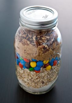 a glass jar filled with lots of candy and nuts on top of a wooden table