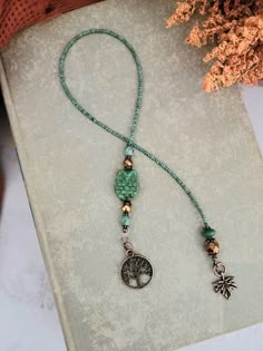 a green beaded necklace with a tree charm on it and a flower in the background