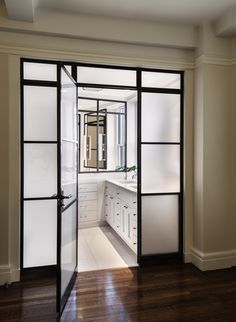 an open door leading to a kitchen with white cabinets and drawers on each side, along with hardwood floors