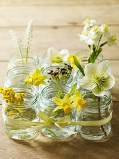 small glass vases with yellow and white flowers in them on a wooden table top