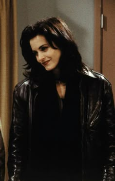 a woman wearing a black leather jacket standing next to a door