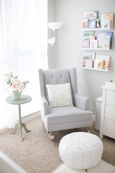 a baby's room with a chair, table and pictures on the wall behind it