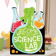 a welcome to the science lab sign in front of a cake and cupcakes