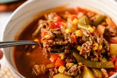 a person holding a spoon full of chili and ground beef soup in a white bowl