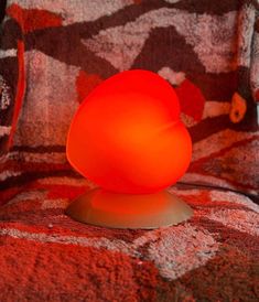 an orange light sitting on top of a red chair next to a pillow and blanket