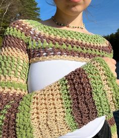 a woman wearing a green, brown and white crochet shawl over her belly