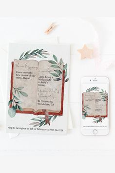 an open book next to a cell phone on a white surface with leaves and branches