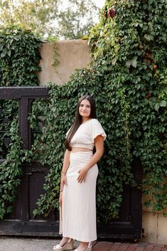 a woman standing in front of a wall covered with green plants and greenery, smiling at the camera