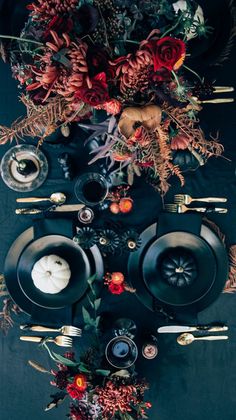 the table is set with black plates, silverware and floral centerpieces on it